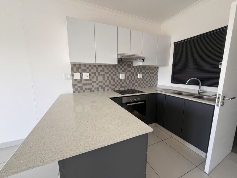 Modern kitchen featuring quartz countertops, dark lower cabinetry, white upper cabinets, built-in oven, electric hob, and a double sink with a tiled backsplash.