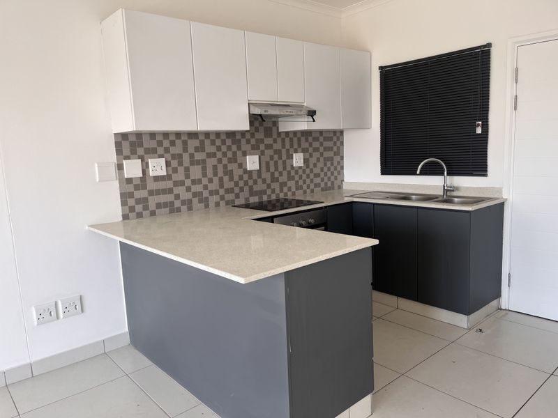 Modern kitchen featuring dark lower cabinets, white upper cabinetry, stone countertops, integrated electric hob, oven, extractor fan, and a double sink with tiled backsplash.