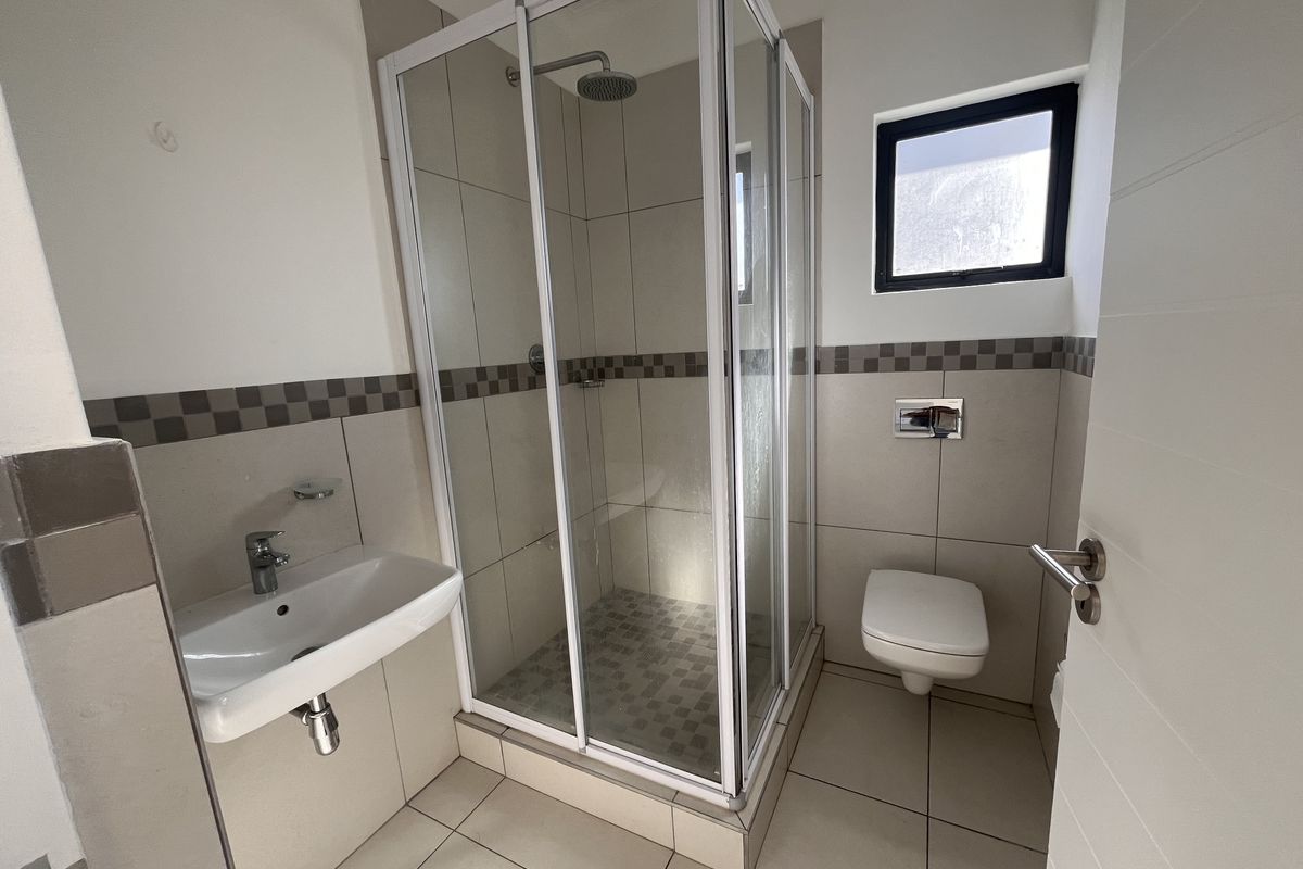 A clean, modern bathroom featuring a glass shower enclosure, wall-mounted toilet, and basin with neutral tiled finishes throughout.