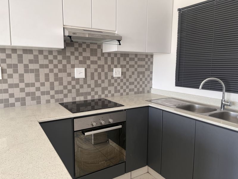 Modern kitchen featuring sleek dark lower cabinetry, white upper cabinets, stone countertops, a built-in oven, electric hob, and a double bowl sink.