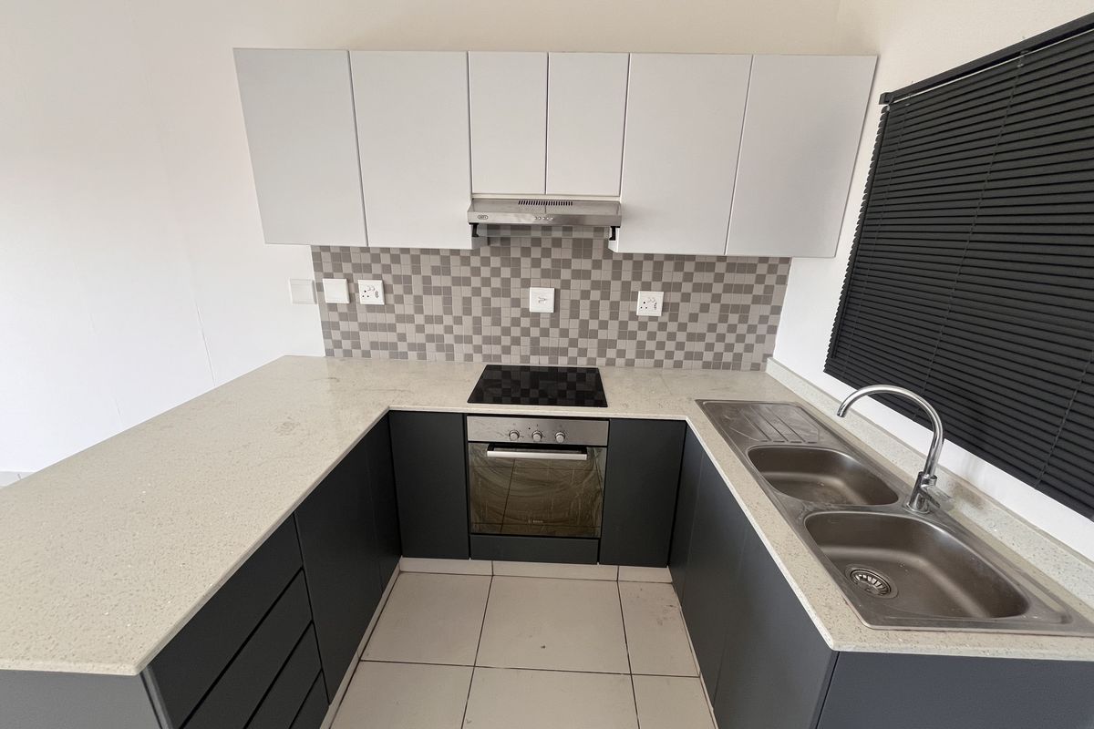 Modern kitchen featuring dark lower cabinetry, white upper cabinets, stone countertops, integrated electric hob, oven, extractor fan, and a double stainless steel sink.