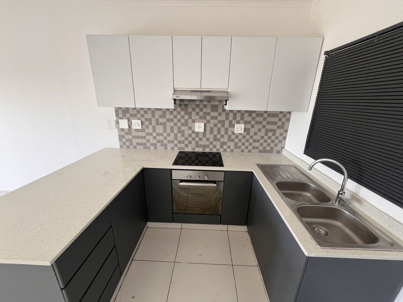 Modern kitchen featuring dark lower cabinetry, white upper cabinets, stone countertops, integrated electric hob, oven, extractor fan, and a double stainless steel sink.