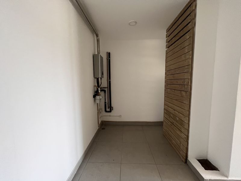 A clean, functional utility space featuring tiled flooring, a wall-mounted gas water heater, and a decorative timber slat screen.