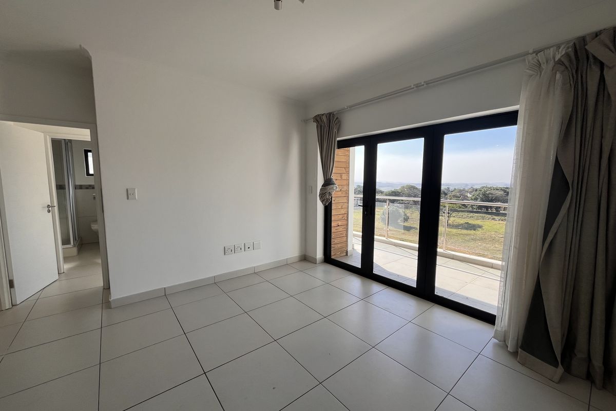 An empty, well-lit living area featuring neutral tiled flooring and large sliding glass doors that open onto a balcony with scenic views.