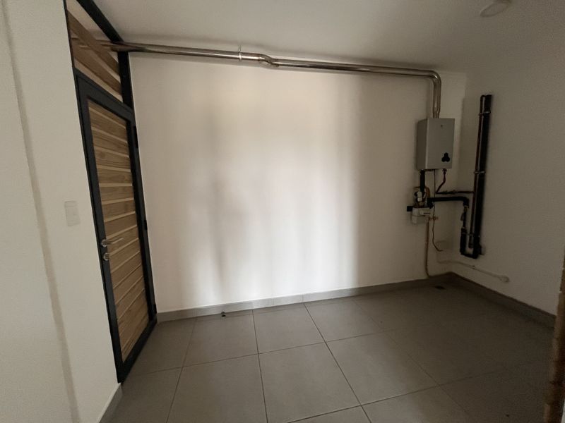 A clean, functional utility space featuring tiled flooring, a wall-mounted gas water heater, and exposed plumbing infrastructure.
