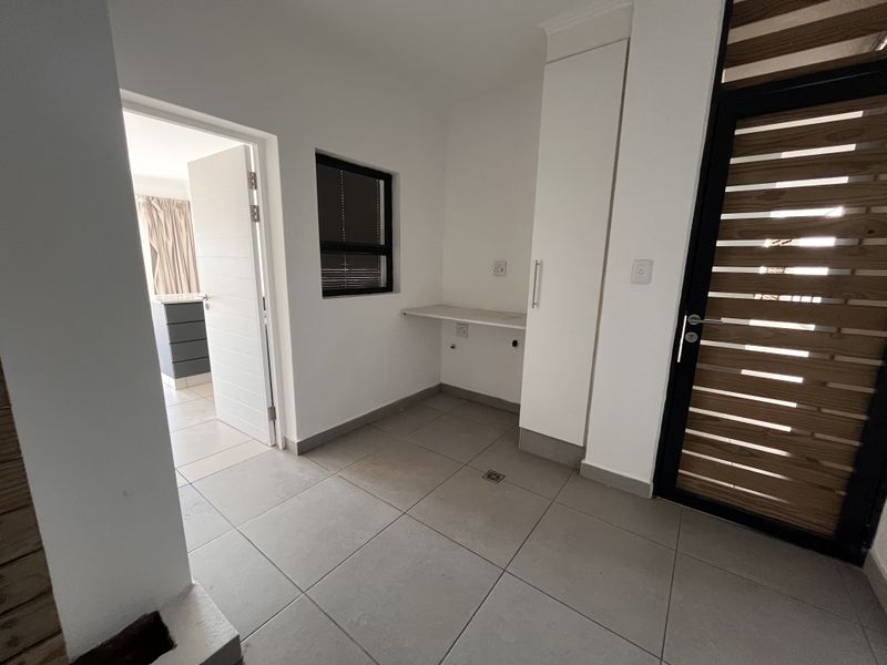 A clean, functional laundry area featuring tiled floors, built-in cabinetry, a countertop, and dedicated plumbing connections for appliances.