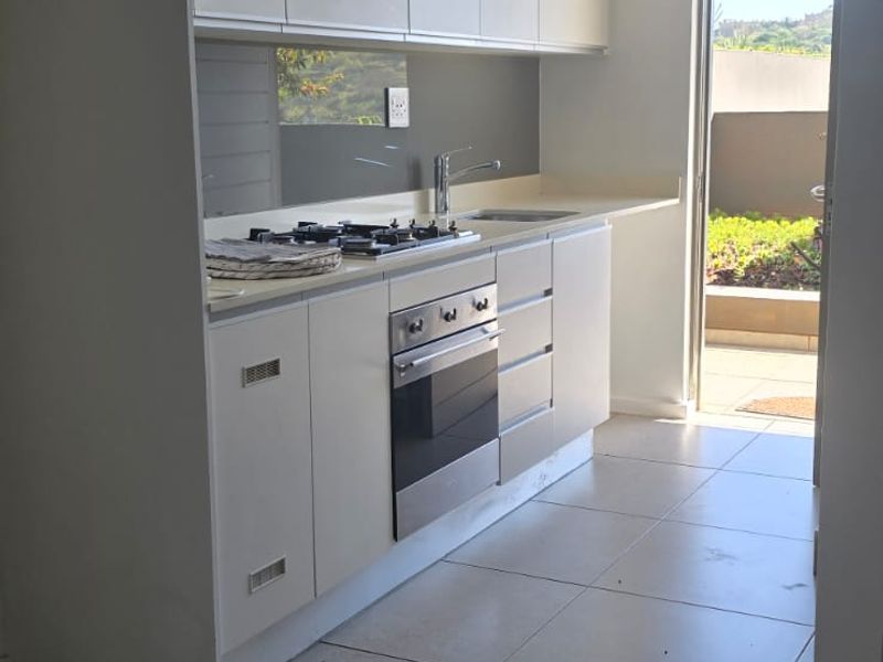 Modern galley-style kitchen featuring white cabinetry, gas cooktop, built-in oven, and tiled flooring, with direct access to an outdoor patio area.