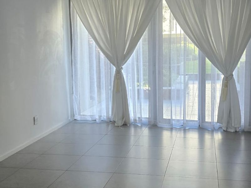 Bright and spacious living area featuring large format floor tiles, a recessed ceiling air conditioning unit, and sliding glass doors leading to the outdoors.