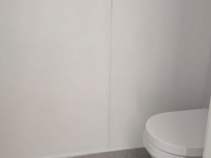 A clean, minimalist bathroom featuring neutral floor tiles and a standard white toilet suite.