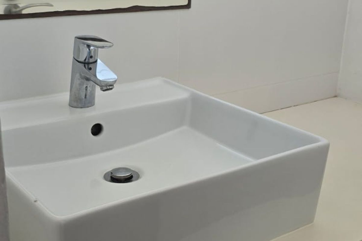 A clean, modern bathroom vanity featuring a white vessel sink, chrome faucet, and a wall-mounted mirror with tiled splashback.