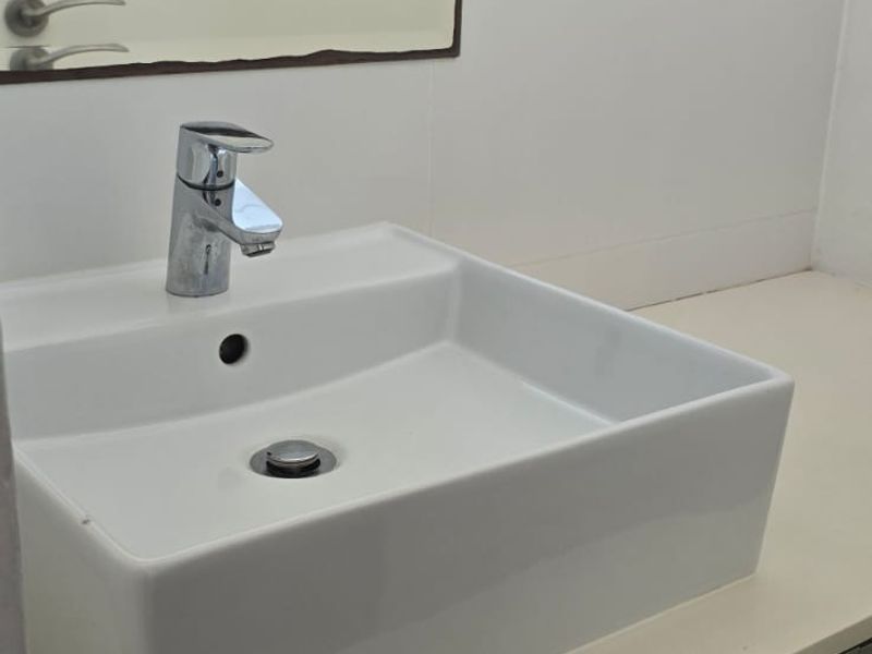 A clean, modern bathroom vanity featuring a white vessel sink, chrome faucet, and a wall-mounted mirror with tiled splashback.
