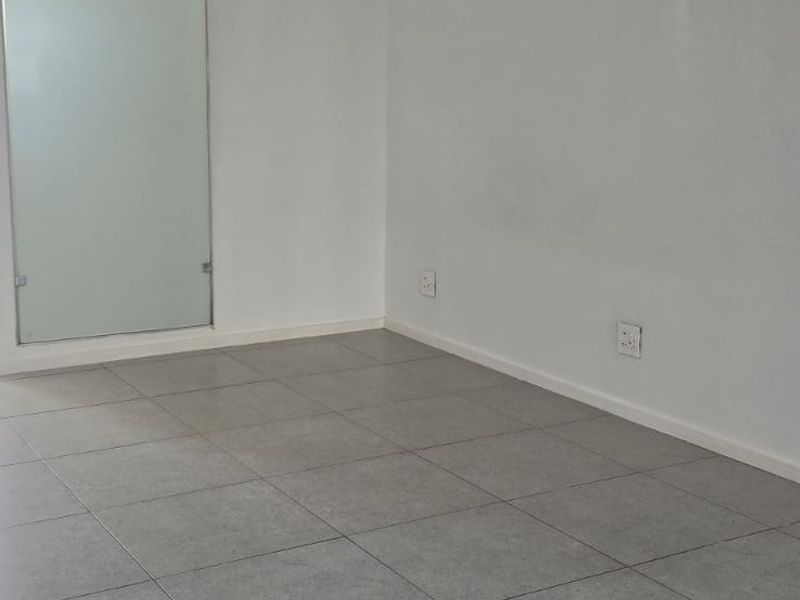 A bright, empty living area featuring modern grey floor tiles, a ceiling-mounted air conditioning unit, and a sleek frosted glass door.