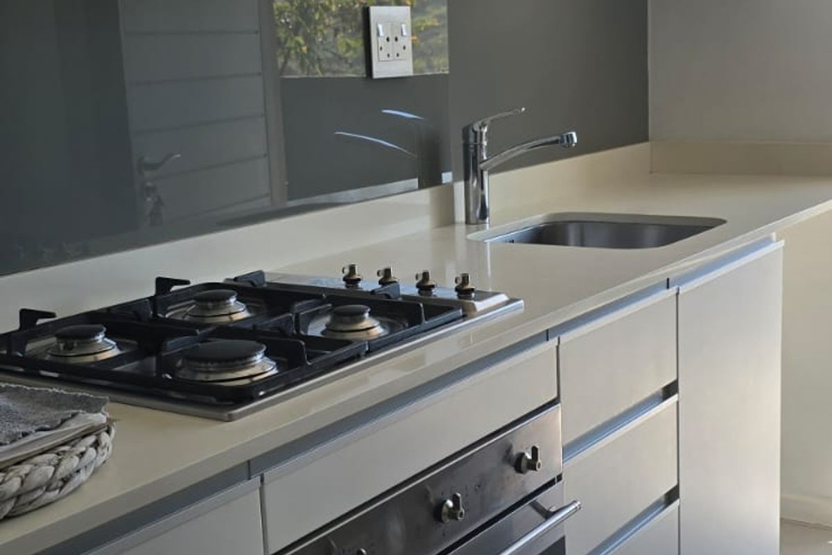 Modern kitchen featuring sleek cabinetry, stone countertops, a gas hob, built-in oven, and a glass splashback with neutral tiled flooring.