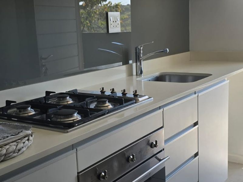 Modern kitchen featuring sleek cabinetry, stone countertops, a gas hob, built-in oven, and a glass splashback with neutral tiled flooring.