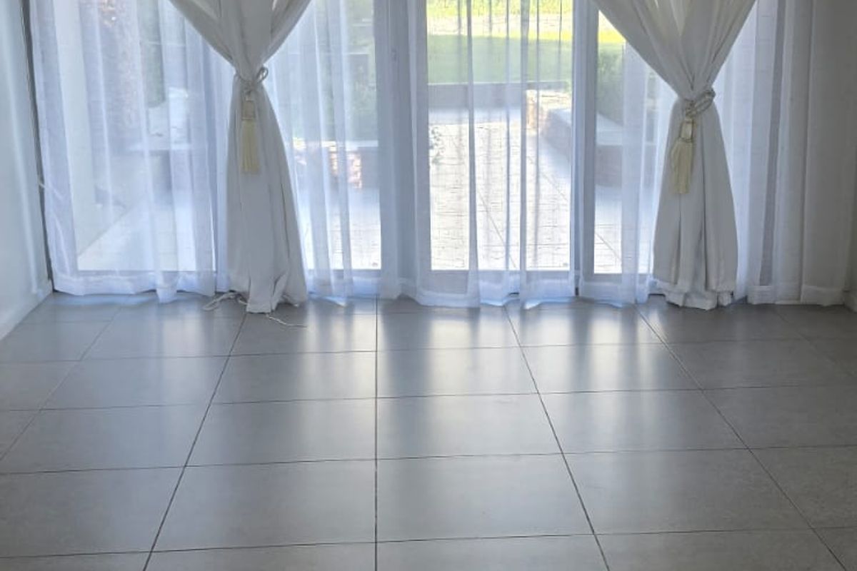 An empty, bright living room featuring large format floor tiles, recessed lighting, a ceiling-mounted air conditioning unit, and sliding glass doors leading outdoors.