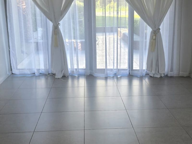 An empty, bright living room featuring large format floor tiles, recessed lighting, a ceiling-mounted air conditioning unit, and sliding glass doors leading outdoors.