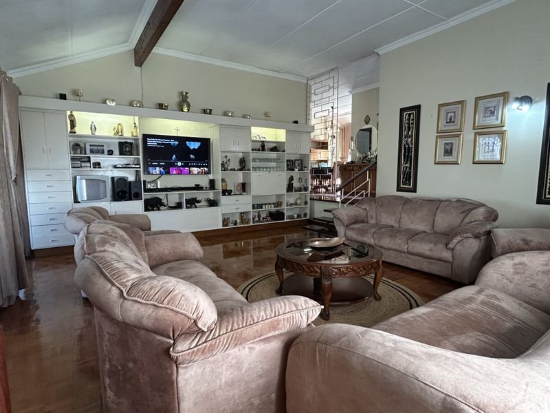Spacious living room featuring extensive built-in cabinetry, parquet flooring, and an exposed ceiling beam, offering a classic and functional layout.