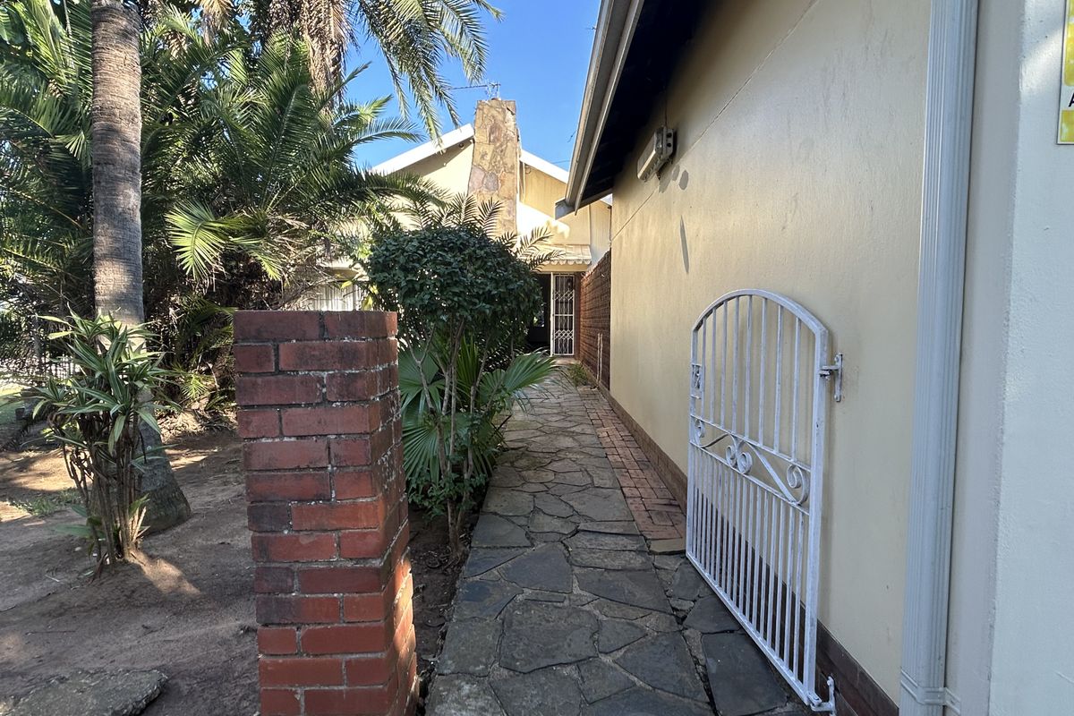 A side walkway featuring stone paving, a brick pillar, and a metal security gate leading towards the rear of the property.