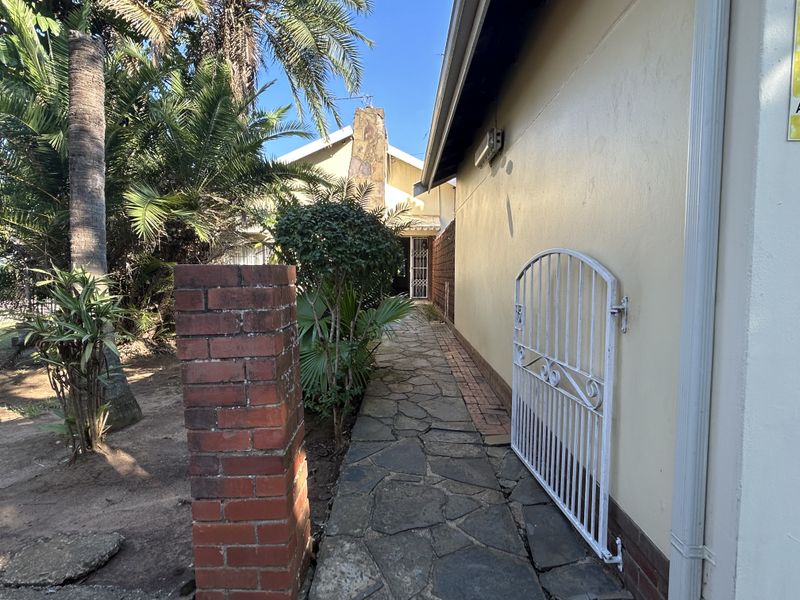 A side walkway featuring stone paving, a brick pillar, and a metal security gate leading towards the rear of the property.