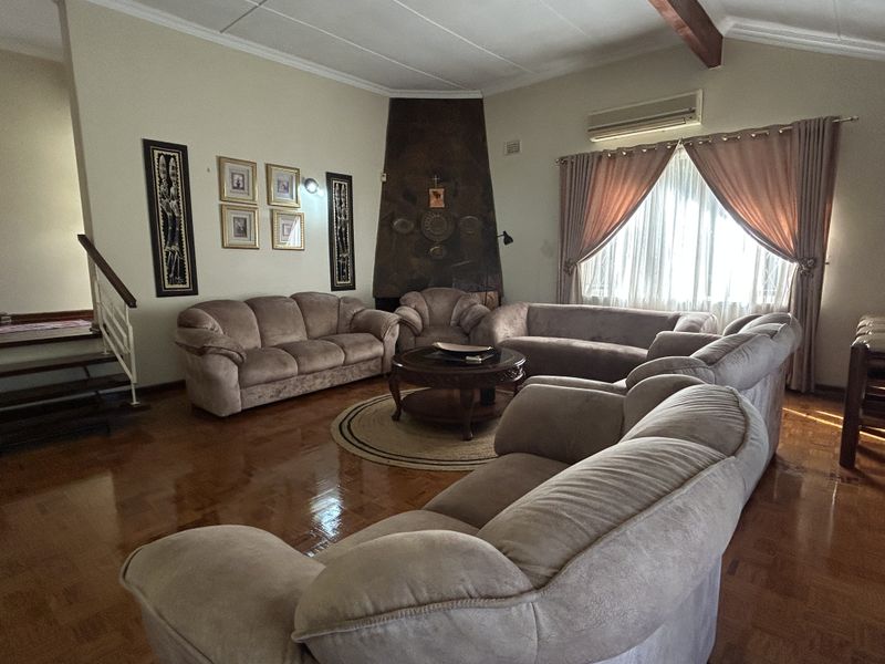 Spacious living room featuring polished parquet flooring, a unique corner fireplace, and a split-system air conditioner, with an adjacent staircase.
