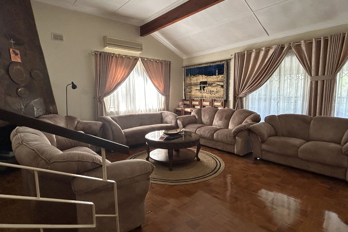 Spacious living room featuring polished parquet flooring, an exposed timber ceiling beam, and a fireplace, offering a comfortable and traditional living space.