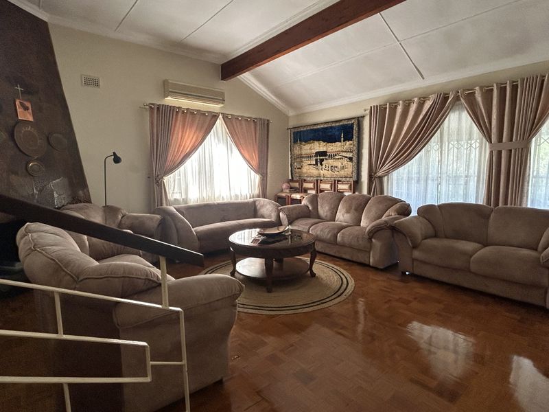 Spacious living room featuring polished parquet flooring, an exposed timber ceiling beam, and a fireplace, offering a comfortable and traditional living space.