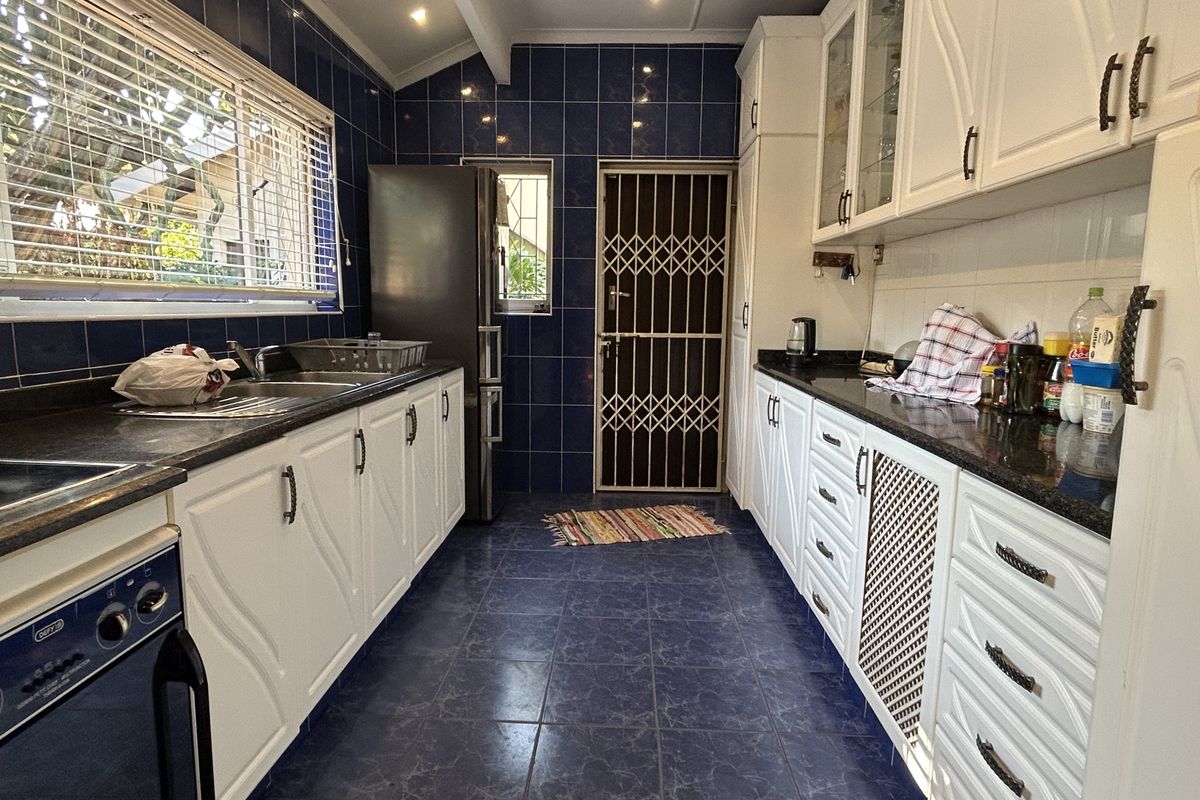 A functional kitchen featuring white cabinetry, dark granite countertops, blue tiled walls and flooring, and a secure rear exit door.