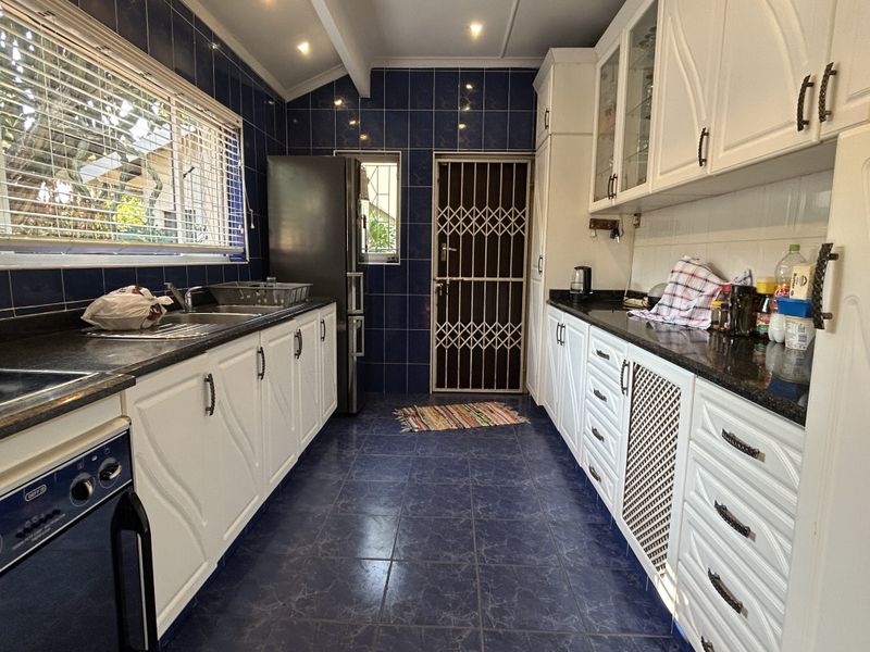 A functional kitchen featuring white cabinetry, dark granite countertops, blue tiled walls and flooring, and a secure rear exit door.