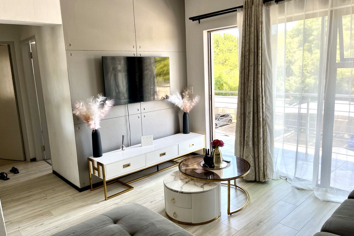 A modern living room featuring light laminate flooring, a decorative feature wall, and a sliding glass door providing access to an outdoor balcony.