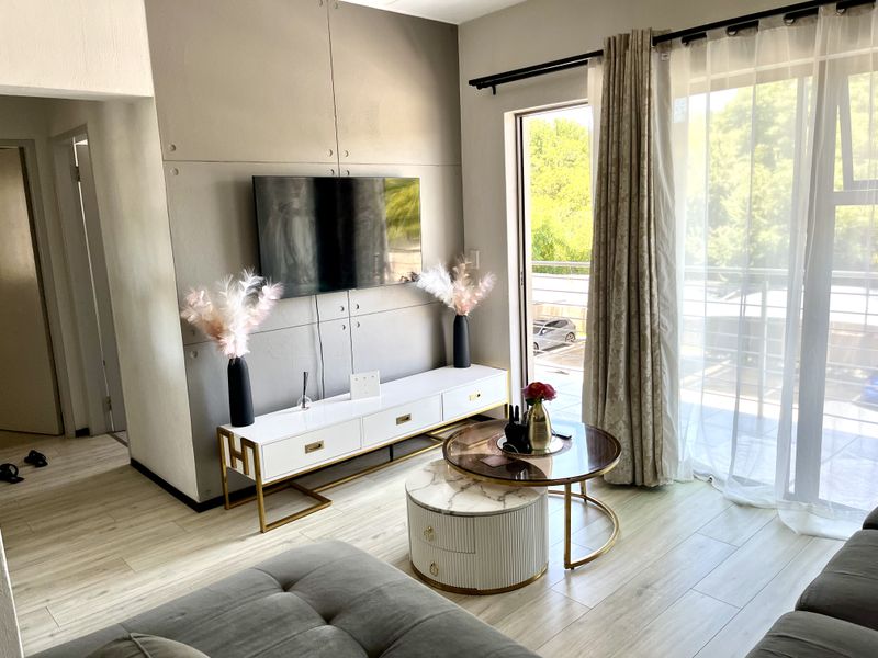 A modern living room featuring light laminate flooring, a decorative feature wall, and a sliding glass door providing access to an outdoor balcony.
