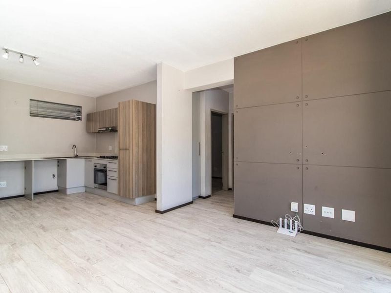 Open-plan living area featuring light laminate flooring, a compact kitchen with built-in oven and hob, and a feature wall with decorative paneling.