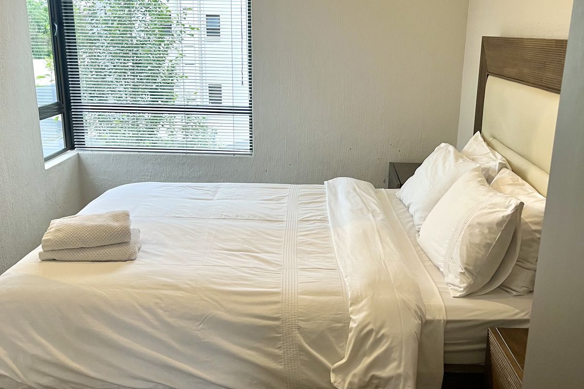 A functional bedroom featuring a corner window with venetian blinds and carpeted flooring.