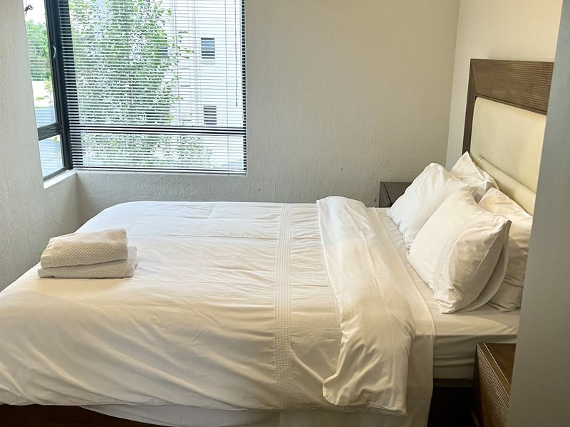 A functional bedroom featuring a corner window with venetian blinds and carpeted flooring.