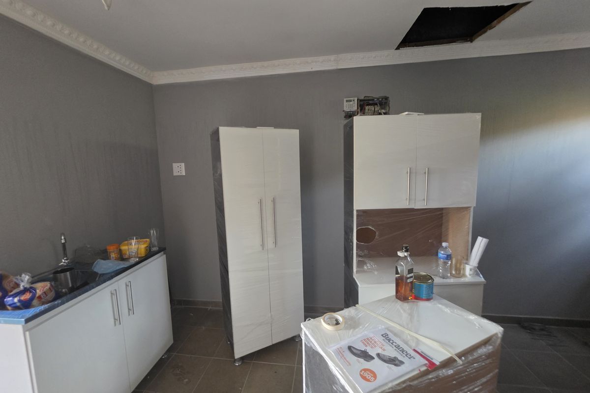 A kitchen space currently undergoing renovation, featuring new white cabinetry, tiled floors, and pending ceiling and electrical finishing work.