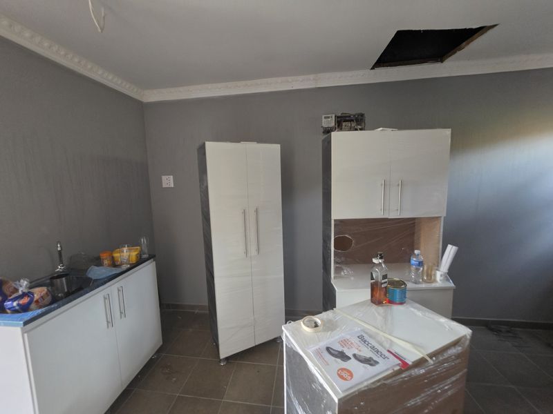 A kitchen space currently undergoing renovation, featuring new white cabinetry, tiled floors, and pending ceiling and electrical finishing work.