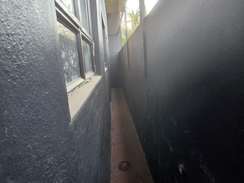 A narrow side passage or exterior walkway featuring dark painted walls, a drainage grate, and a window.