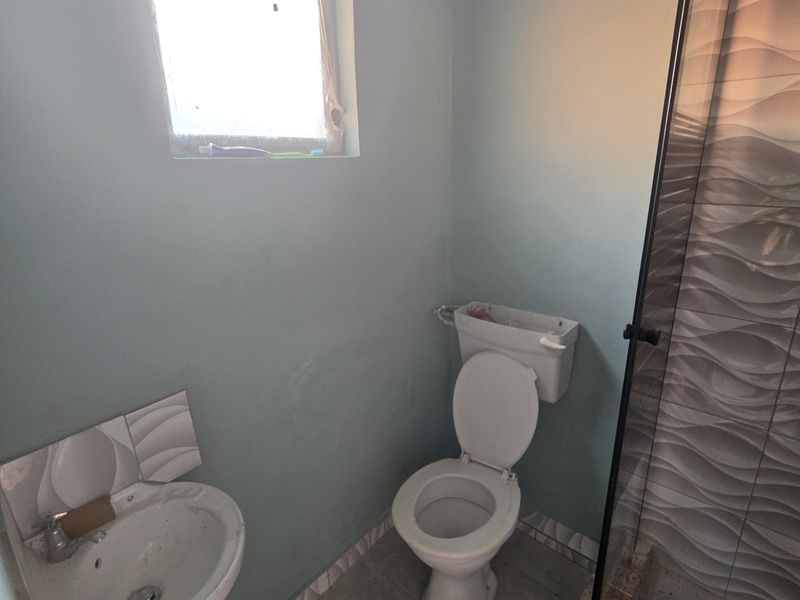 A compact bathroom featuring a wall-mounted basin, toilet, and a shower enclosure with decorative tiled walls.