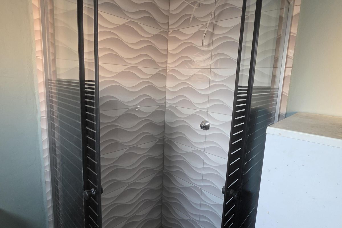 A bathroom shower enclosure featuring decorative wave-patterned wall tiles, currently requiring installation of shower fixtures and completion of electrical work.