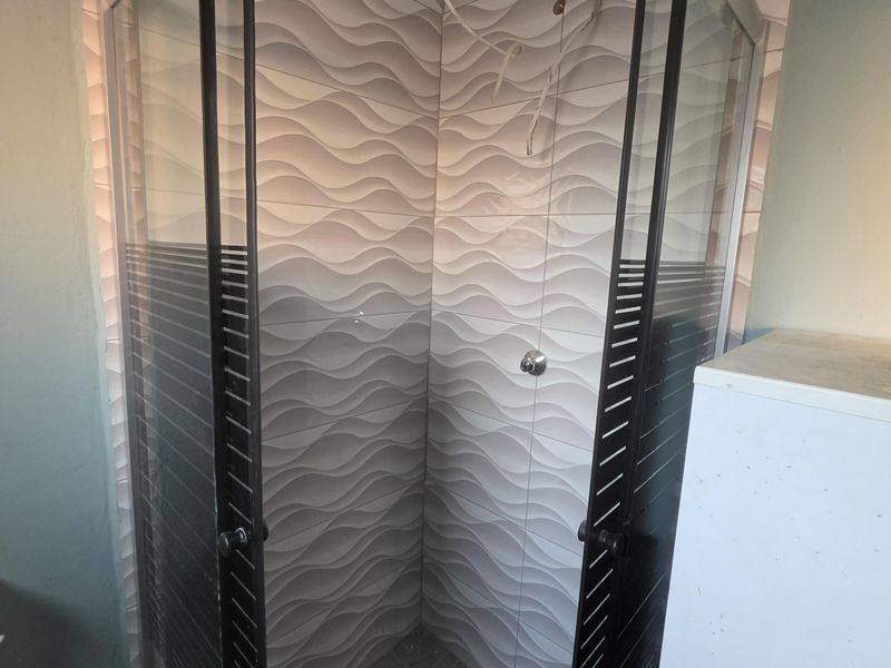 A bathroom shower enclosure featuring decorative wave-patterned wall tiles, currently requiring installation of shower fixtures and completion of electrical work.