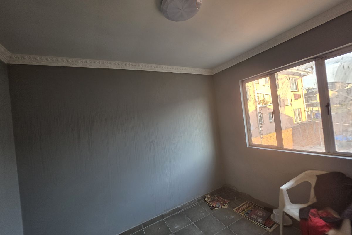 An empty bedroom featuring tiled flooring, ceiling cornice, and a flush mount light fixture, with visible wall paint streaking requiring attention.