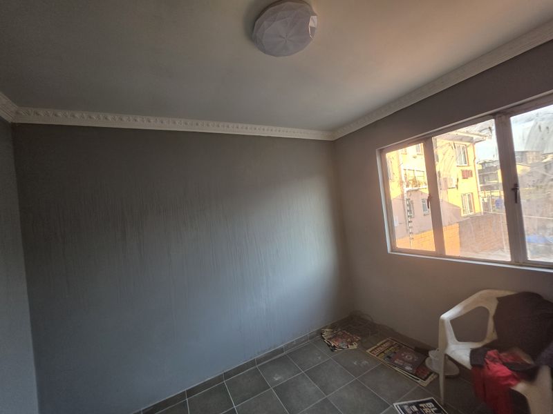 An empty bedroom featuring tiled flooring, ceiling cornice, and a flush mount light fixture, with visible wall paint streaking requiring attention.