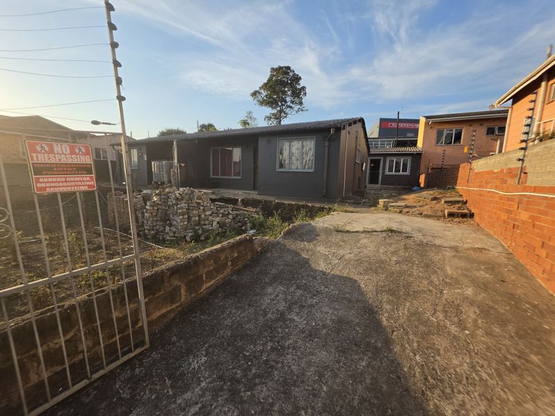 Front exterior view of a residential property featuring a concrete driveway, security fencing, and ongoing site work with visible construction materials.