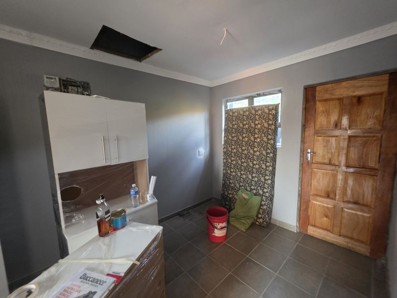 A utility space featuring tiled flooring, built-in cabinetry, and a wooden door, currently requiring repairs to the ceiling and electrical fixtures.