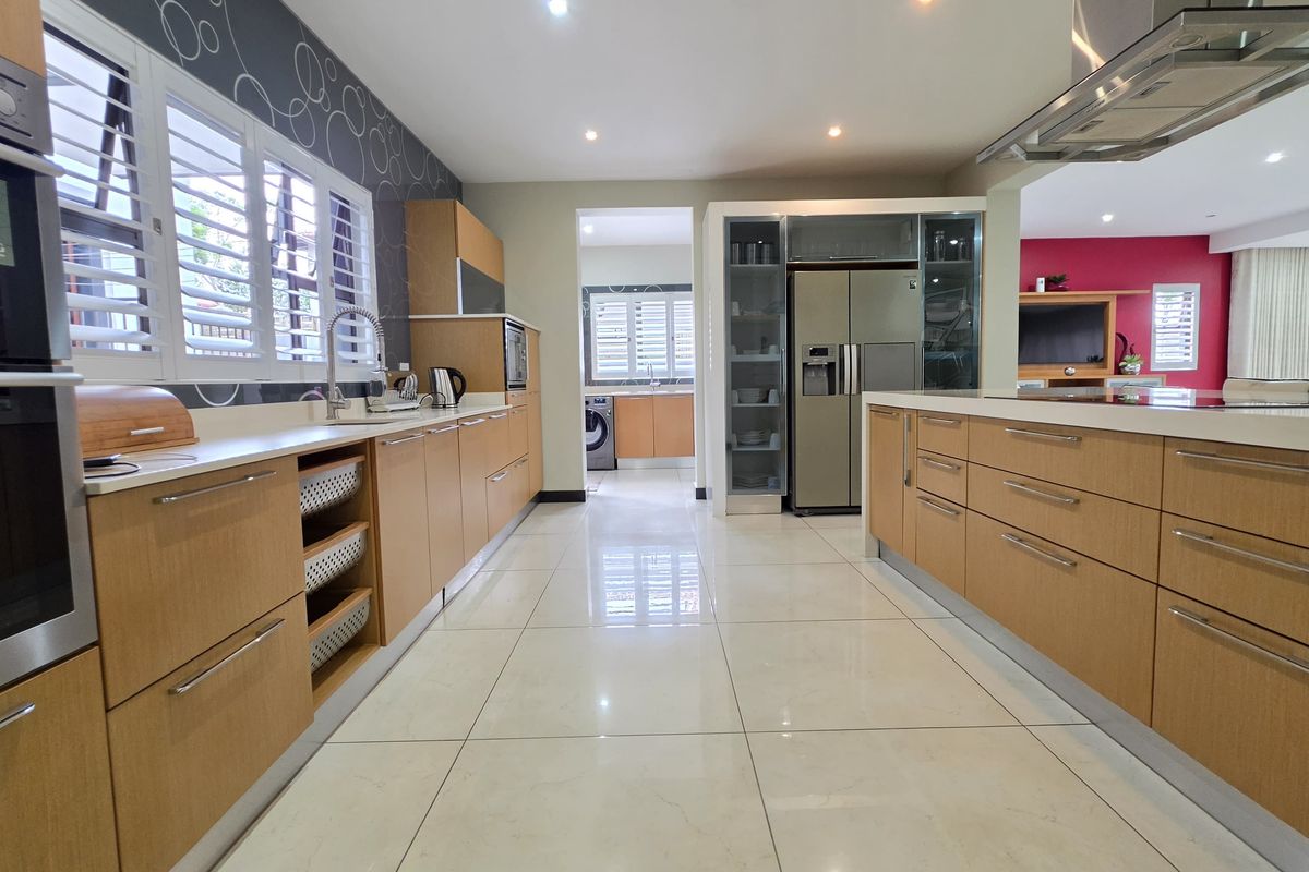 Modern kitchen featuring light wood cabinetry, stone countertops, a central island, and integrated appliances, with a seamless flow into the adjacent living area.