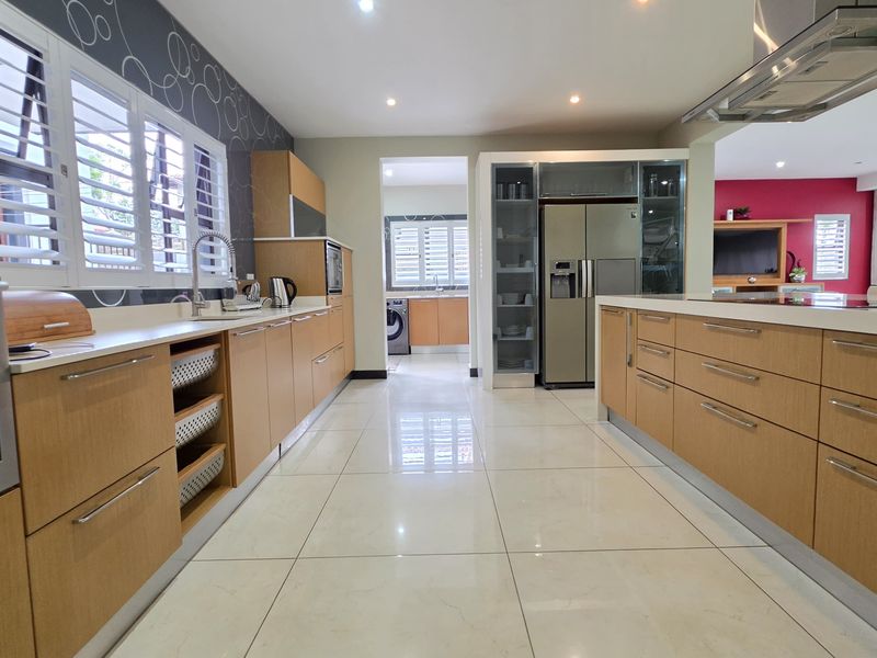 Modern kitchen featuring light wood cabinetry, stone countertops, a central island, and integrated appliances, with a seamless flow into the adjacent living area.