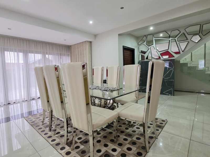 Modern dining area featuring polished tiled flooring, recessed lighting, and a contemporary glass staircase balustrade, creating an open and bright atmosphere.