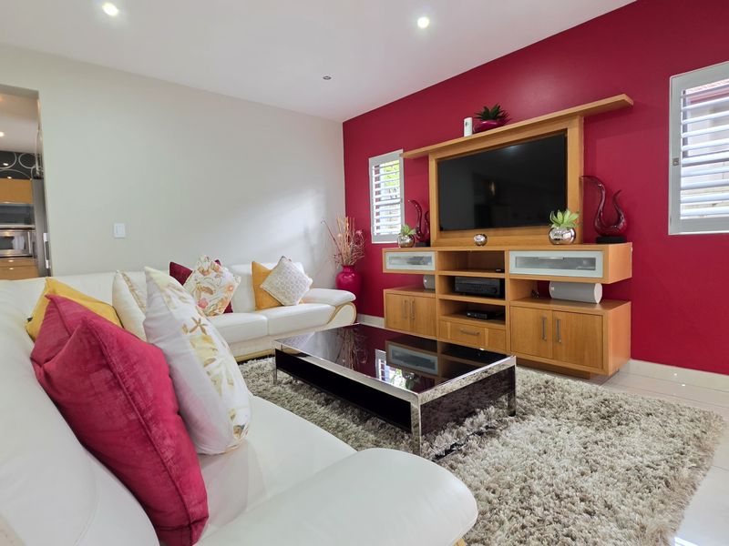 Open-plan living area featuring tiled flooring, recessed lighting, and a built-in media unit, with an adjacent kitchen visible in the background.