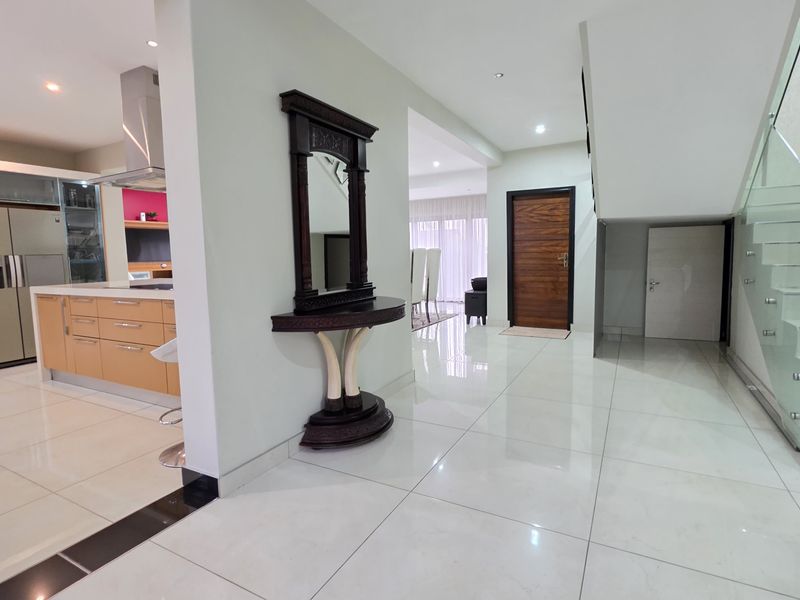 Spacious open-plan entrance hall featuring polished porcelain tiles, a modern glass-railed staircase, and a seamless transition into the contemporary kitchen area.