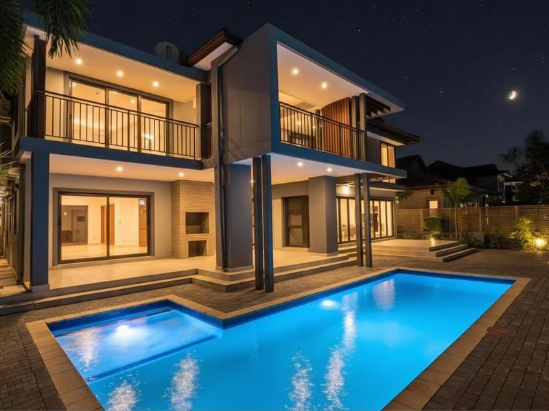 Modern double-story residence featuring a spacious covered patio, upper-level balcony, and a well-lit swimming pool area, perfect for evening outdoor entertaining.
