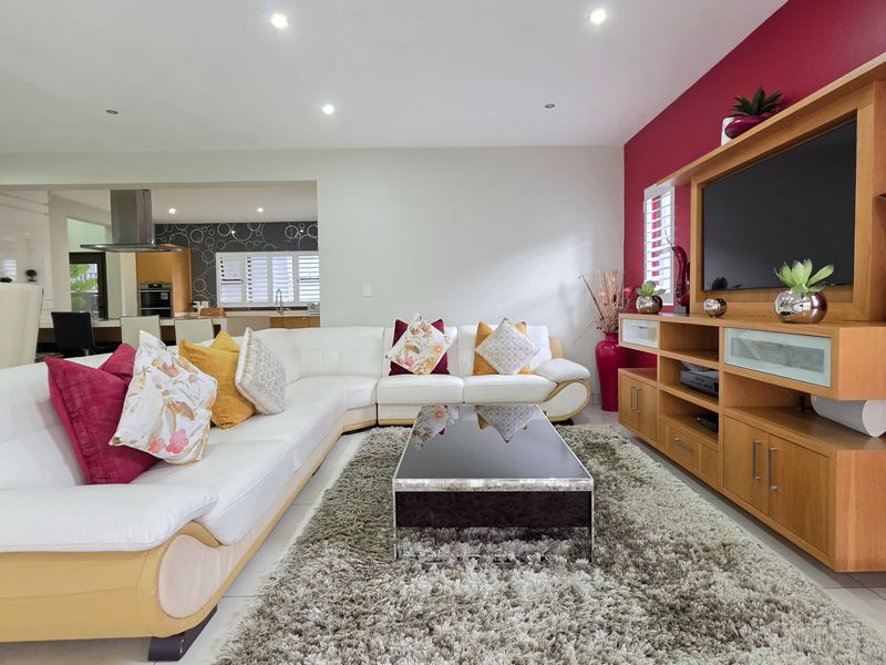 Spacious open-plan living area featuring tiled flooring, recessed lighting, and a built-in media unit, seamlessly connecting to the kitchen space.